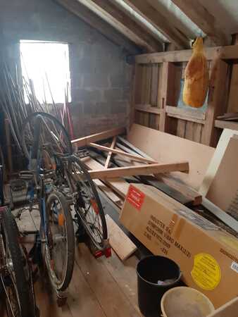 Ein Dachboden mit alten Fahrrädern, Holzbalken, Kartons und einem aufgehängten Schinken.